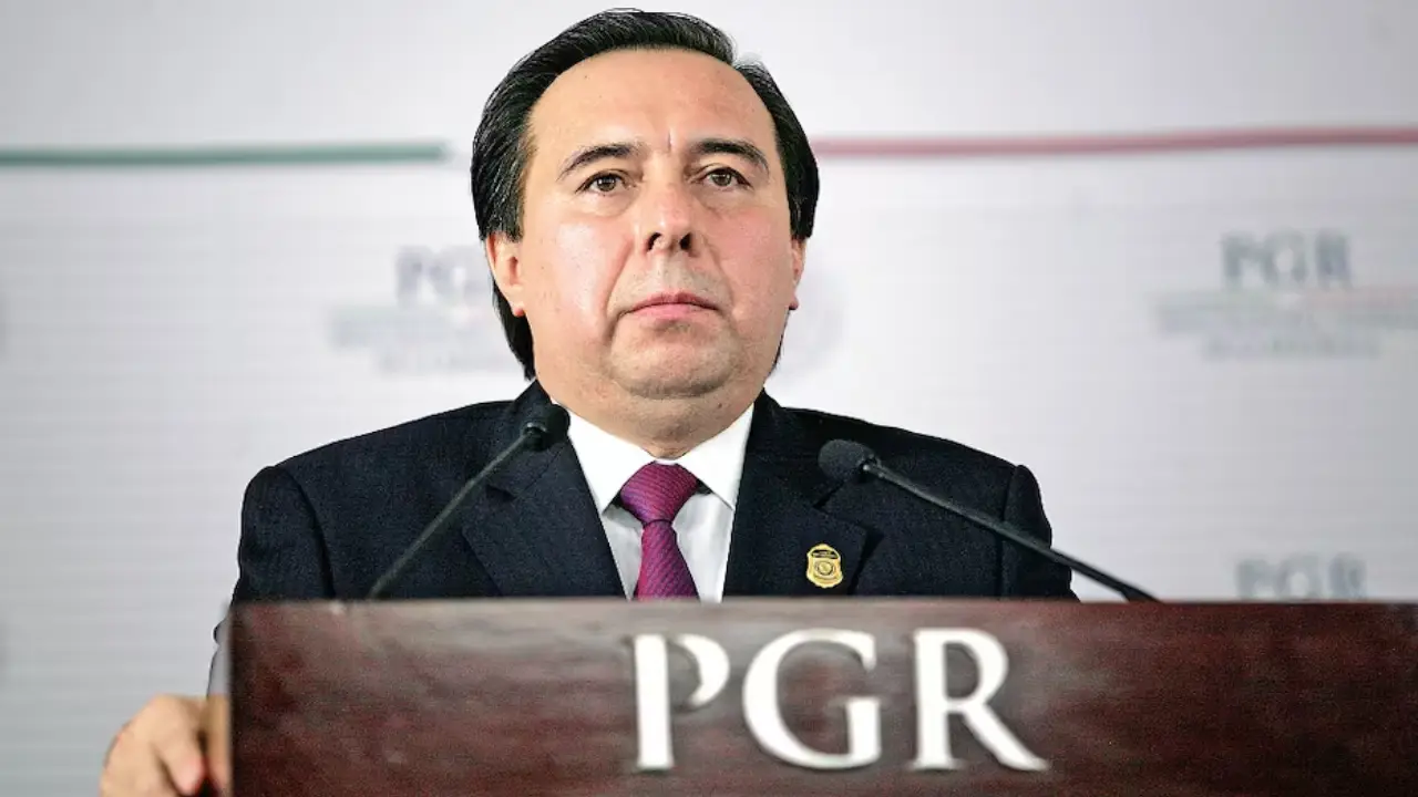 Tomás Zerón de Lucio | México Ahora Man in a dark suit and pink tie speaks at a podium labeled PGR flanked by two microphones