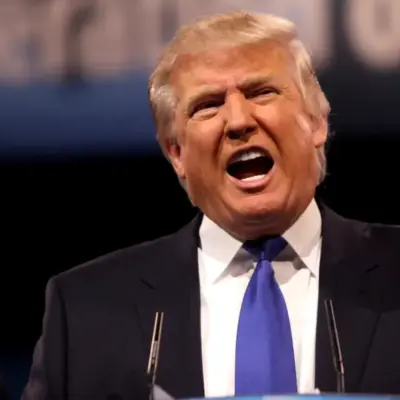 ataque-donald-trump | México Ahora Man in a dark suit and blue tie shouting into a microphone at a podium with one hand raised in a gesturing pose