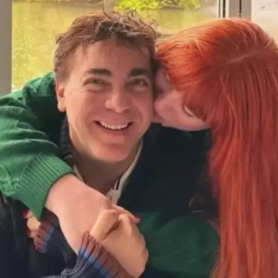 romance de Cristian Castro | México Ahora Couple hugging affectionately woman with red hair kisses man on the cheek while he smiles at the camera