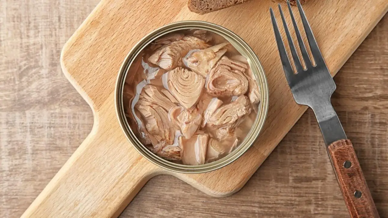 Atún enlatado | México Ahora Open can of tuna in oil resting on a wooden cutting board with a fork nearby