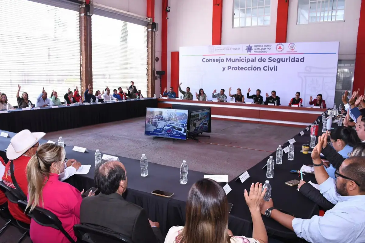 consejo-de-seguridad-atenco | México Ahora Large U shaped conference room with municipal officials raising hands at a Seguridad y Protección Civil meeting banner in the background water bottles on the table
