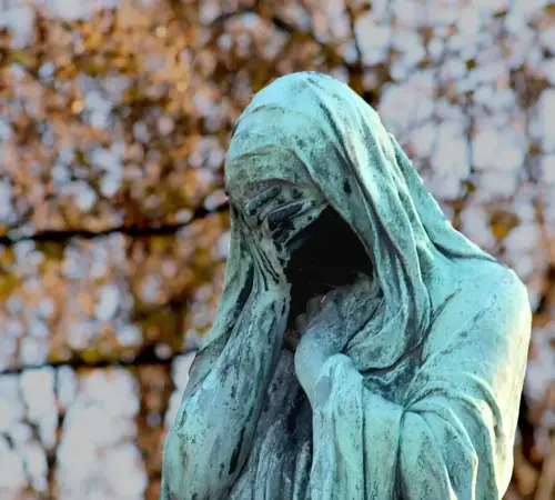 Día Internacional Viudas Día Internacional de las Viudas por qué se conmemora este 23 de junio y cuál es su importancia | Bronze statue of a hooded figure covering its face green patina with autumn foliage in the background
