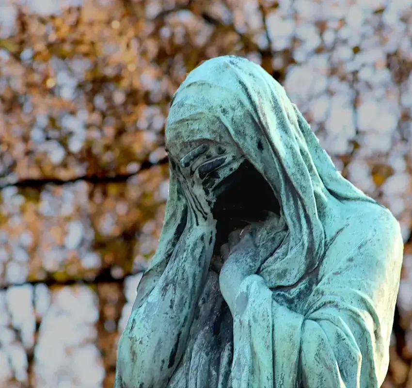 Día Internacional Viudas Día Internacional de las Viudas por qué se conmemora este 23 de junio y cuál es su importancia | Bronze statue of a hooded figure covering its face green patina with autumn foliage in the background