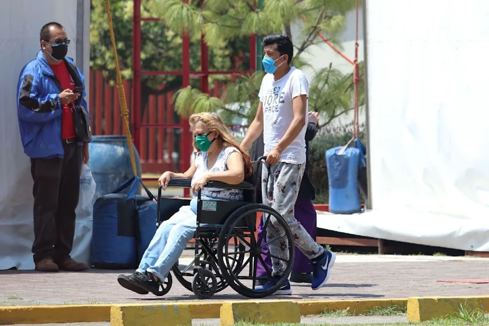 jovenes que cuidan | México Ahora A woman in a wheelchair being pushed by a man as they walk outdoors all wearing masks