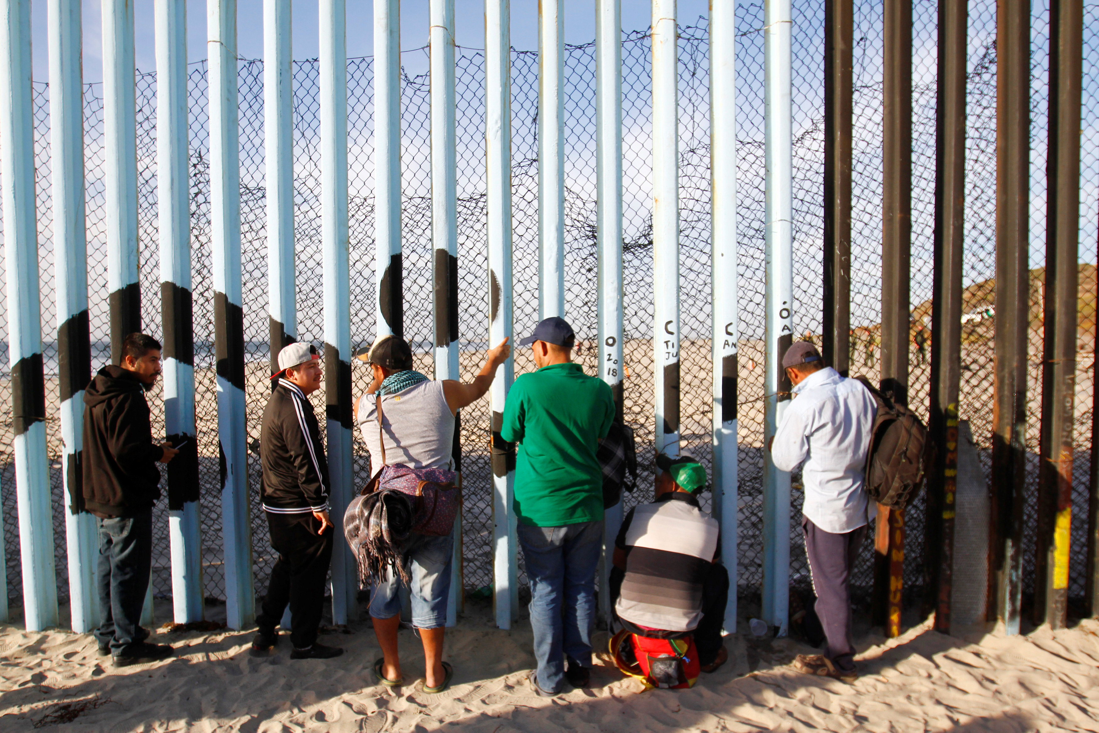 Miembros de la caravana migrante que intenta llegar a EEUU observan a través del vallado fronterizo en Tijuana, Mexico (REUTERS/Jorge Duenes)