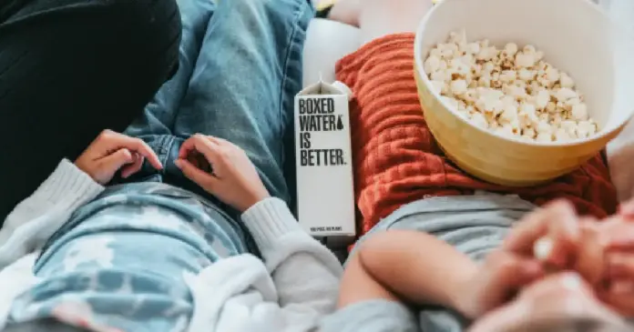 personas sentadas en un sillón con palomitas y botella de agua Con un poco de creatividad, es posible convertir estos días en una experiencia igual de placentera.
