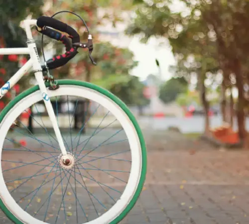 White bicycle with a green front wheel parked on a park path beside trees and a curb